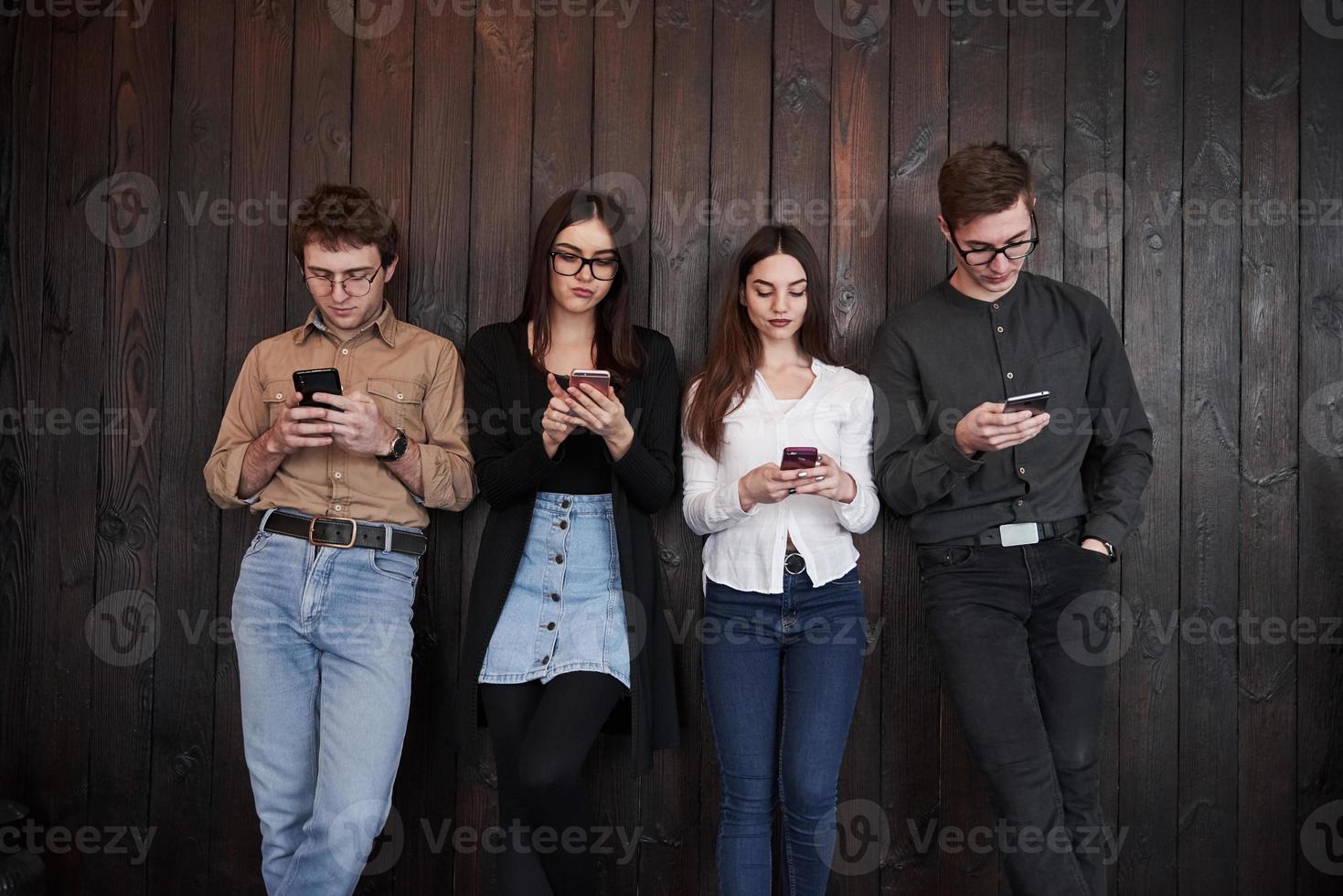 Relaxed and calm. Youth stands against black wooden wall. Group of friends spending time together photo
