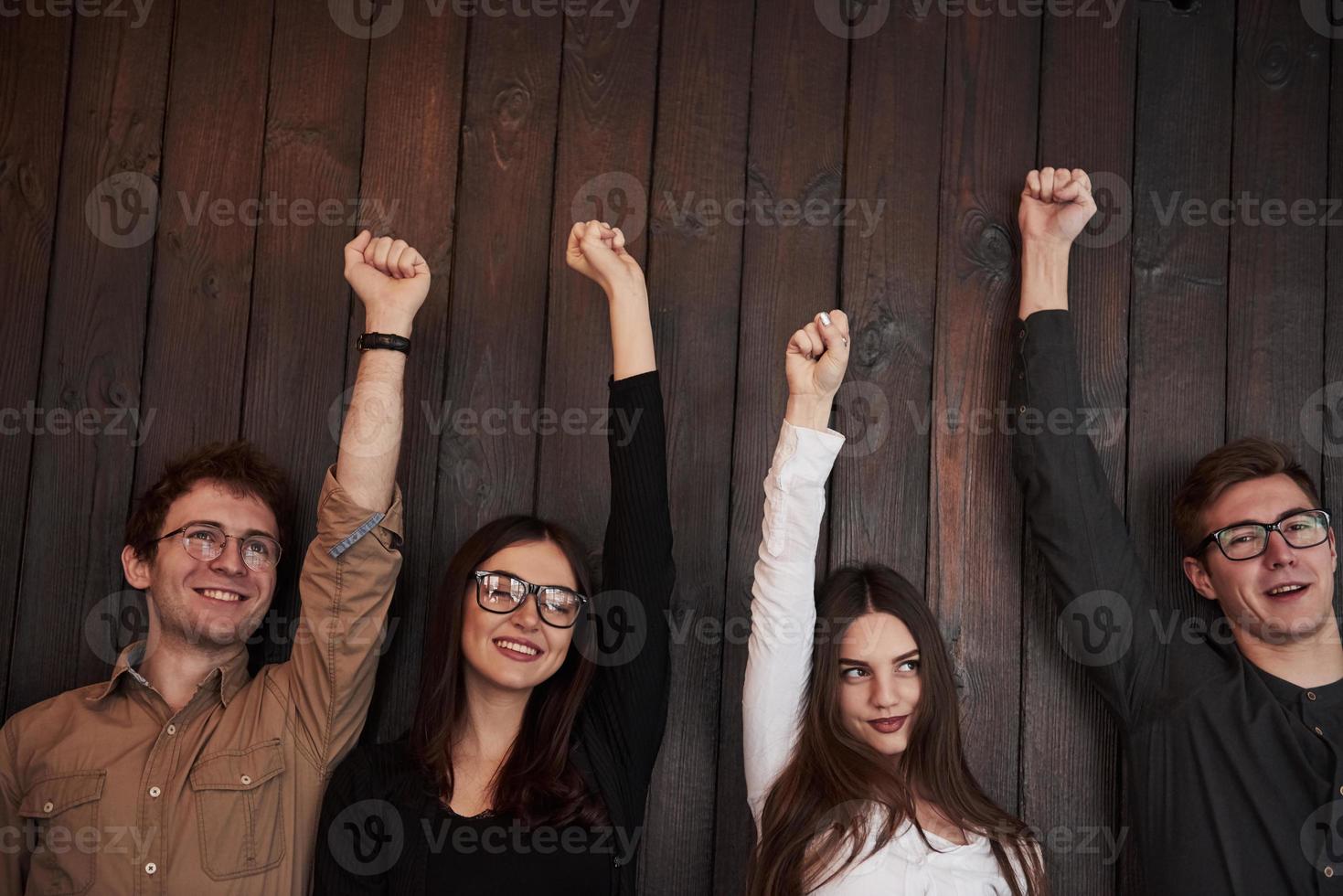 Everyone is happy. Celebrating succeess. Friends put their hands up against black wooden wall photo