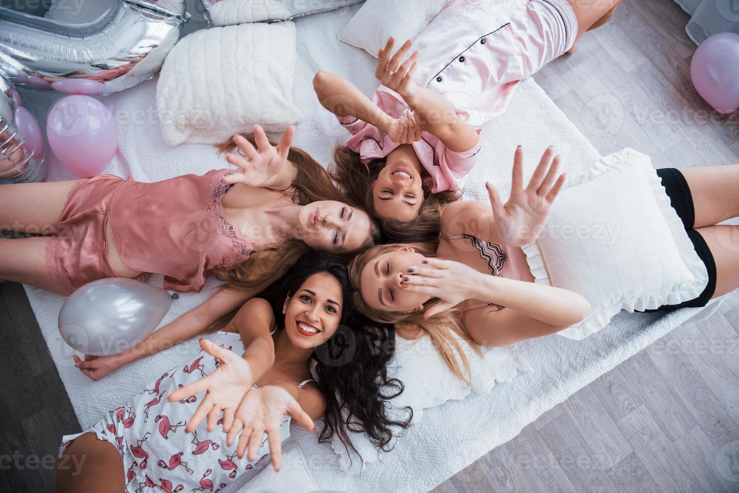 These beautiful friends wish you happy holidays. Top view of young girls at bachelorette party lying on the sofa and raising their hands up photo