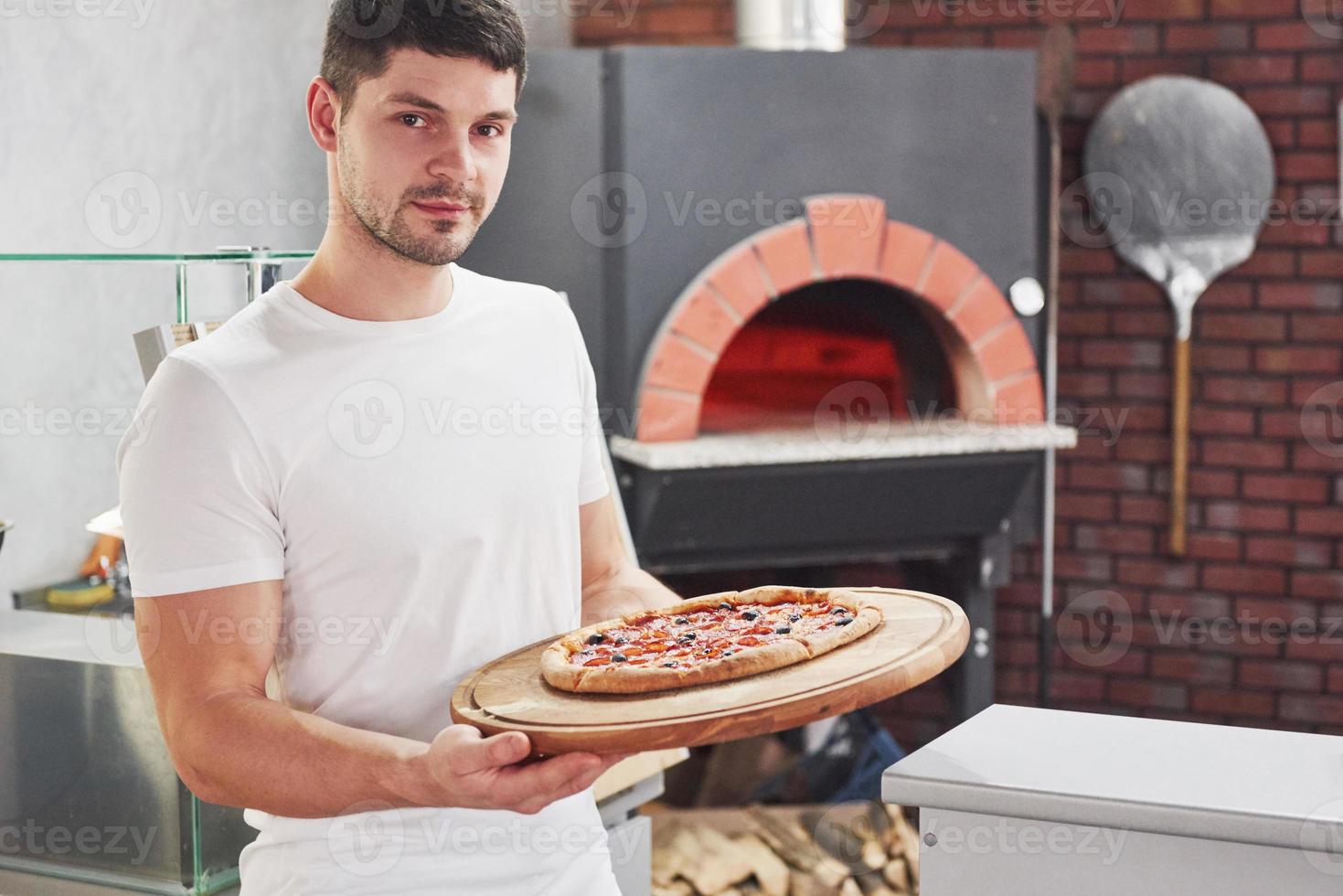 Job well done. Baker in white shirt with pizza that ready for put in the oven to cook photo