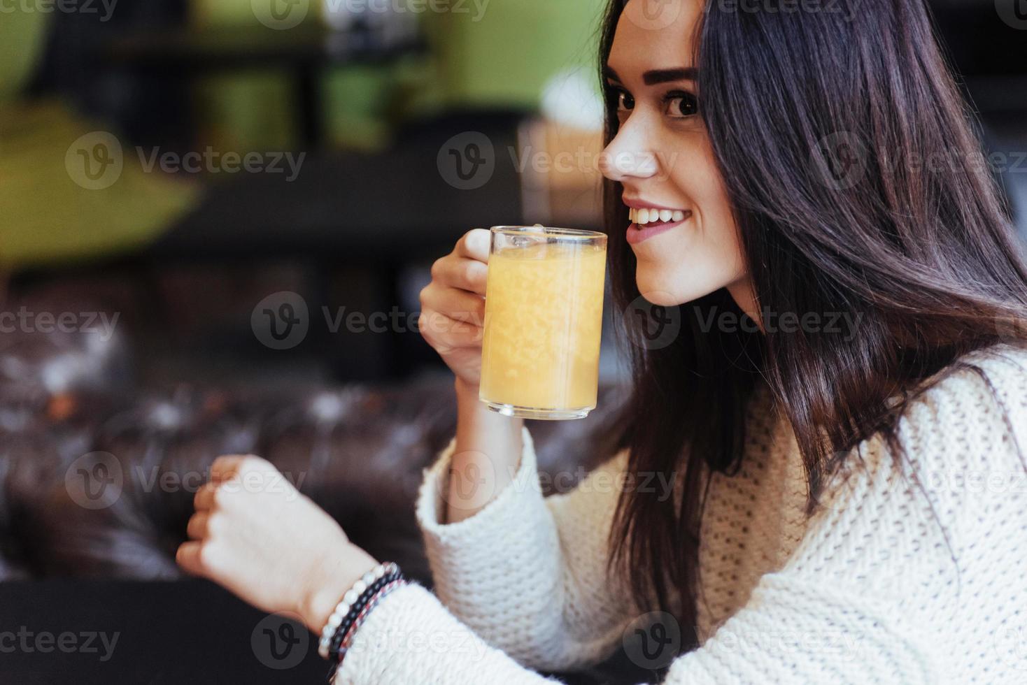 joven morena atractiva y divertida bebe jugo de naranja en el restaurante foto