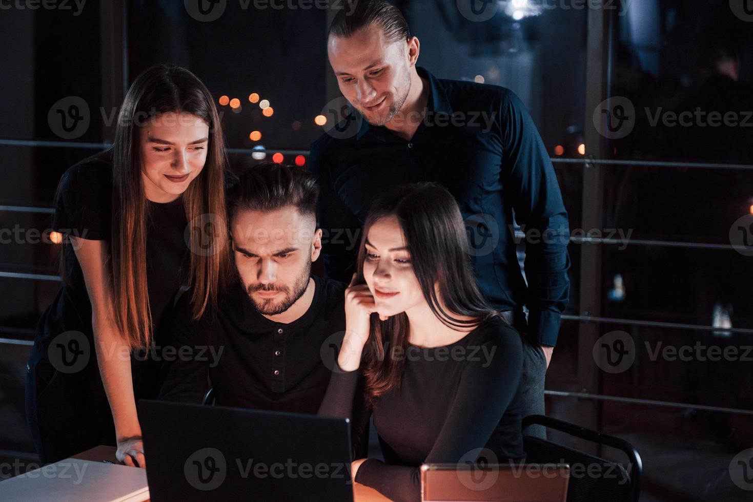 Only man with beard is serious. Team of young business people works on their project at night time in the office photo