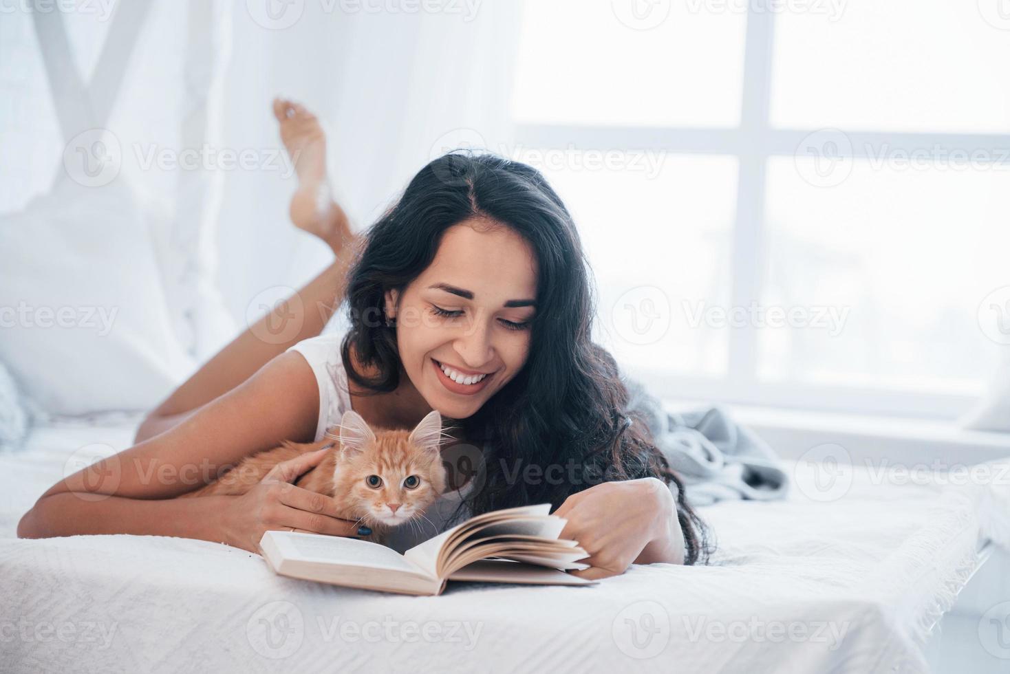 Home calm. Attractive blonde resting on the white bed with her cute kitten photo