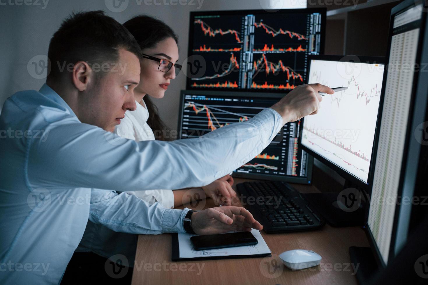 Planning the business project. Team of stockbrokers are having a conversation in a office with multiple display screens photo