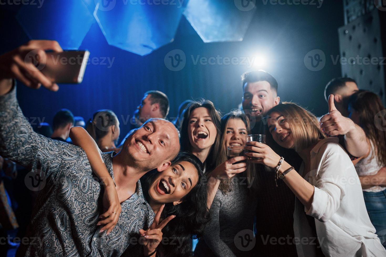 pulgar y alcohol arriba. amigos tomando selfie en una hermosa discoteca. con bebidas en las manos foto