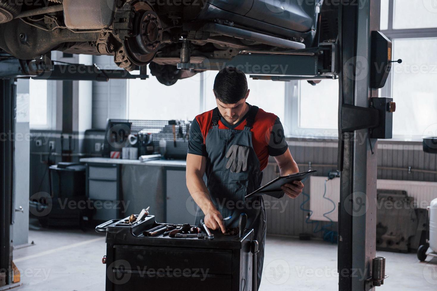 Choosing right instrument. Man at the workshop in uniform fixes broken parts of the modern car photo