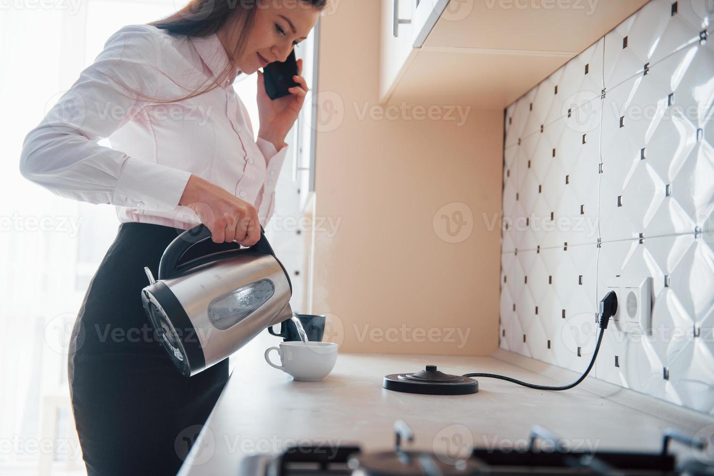 Having conversation and pouring water. Young businesswoman with black hair in official clothes at her home photo