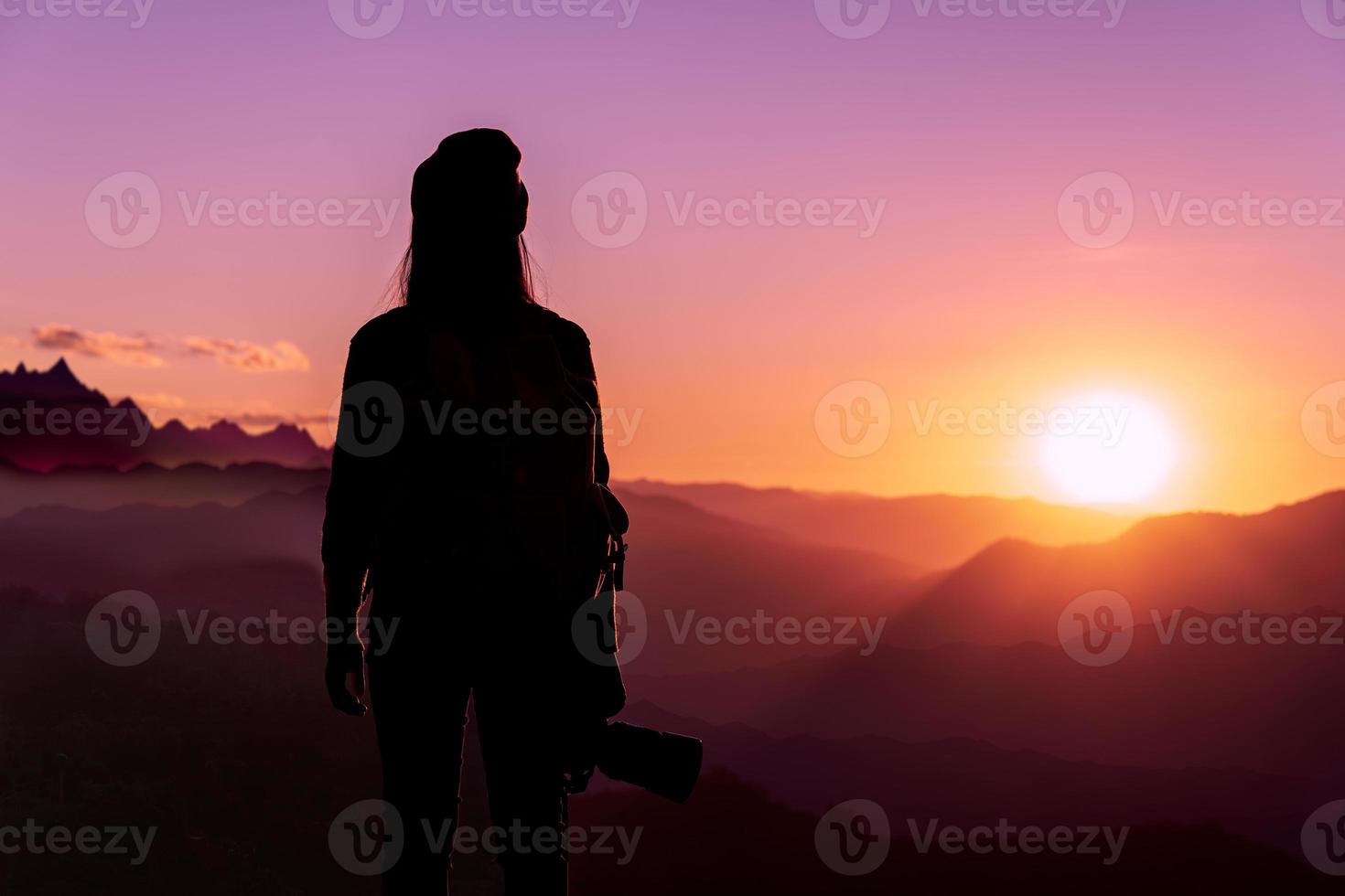 Back view of young hipster photographer holding the camera with sunset on mountain natural background. photo