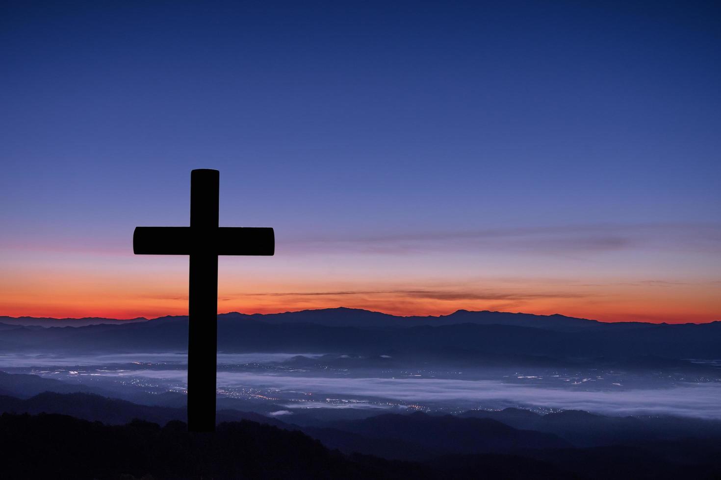 silueta de cruz sobre fondo de amanecer de montaña. foto