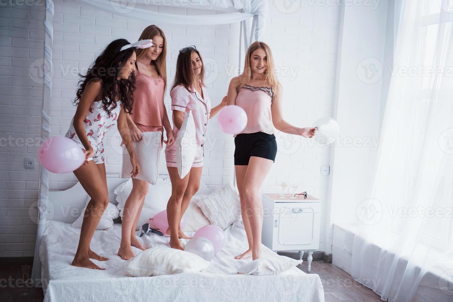 Standing on the luxury white bad at holiday time with balloons and bunny ears. Four beautiful girls in night wear have party photo