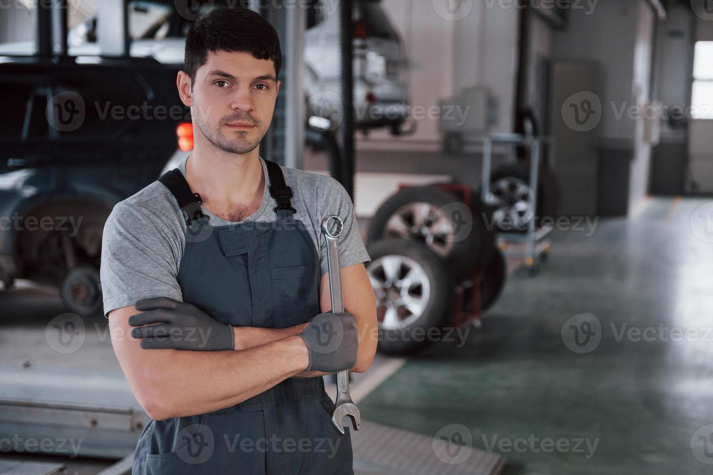 Waiting for customer. Portrait of serious worker in uniform that stands in his workshop with wrench in hand photo