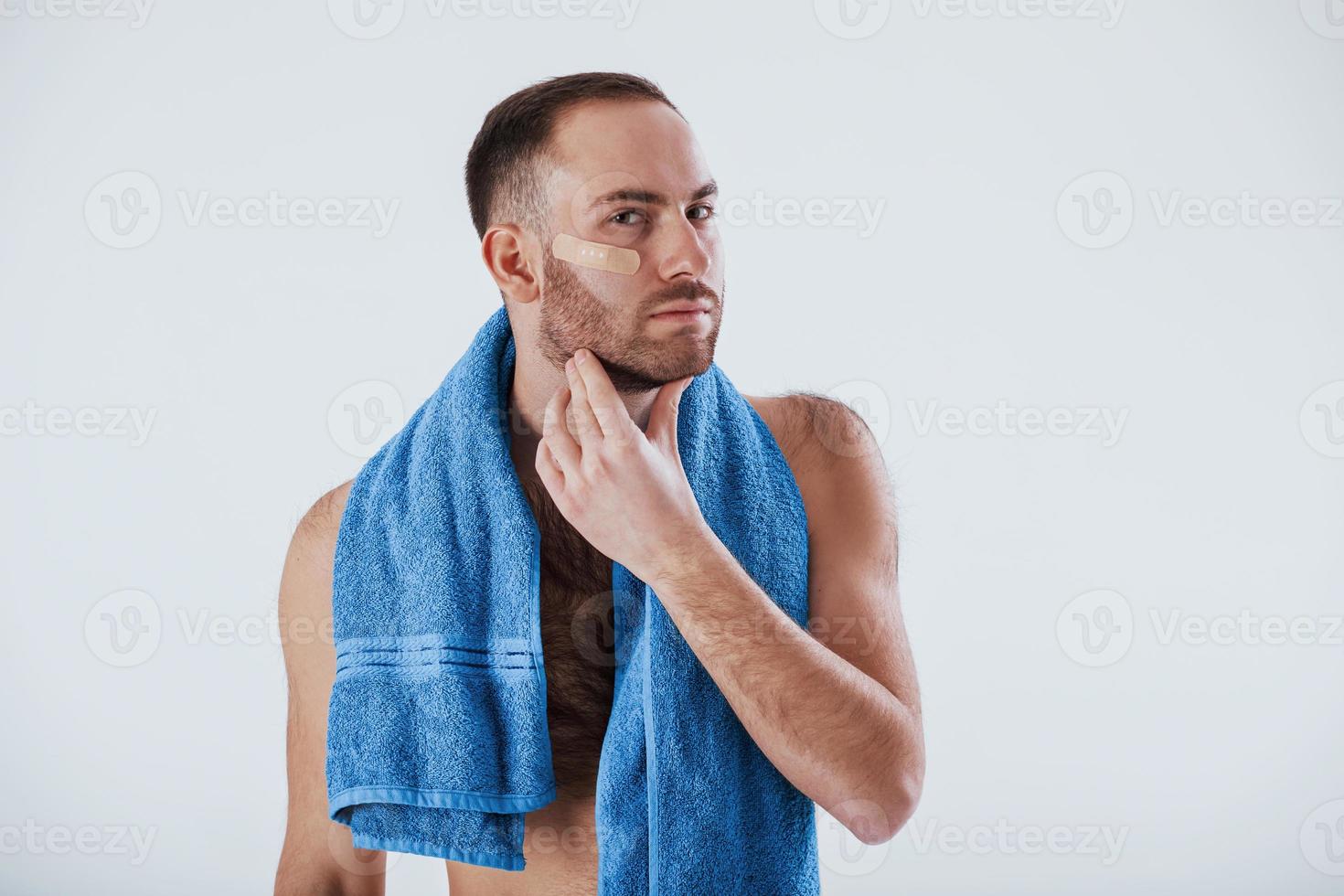 Nice clean skin. Man with blue towel stands against white background in the studio photo