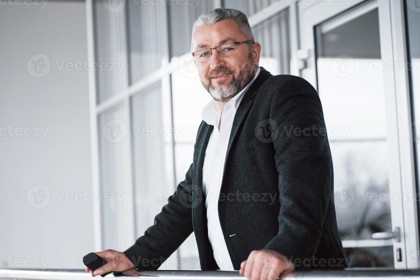 Nice person. Photo of senior businessman in the spacious room. Holding phone and smiling