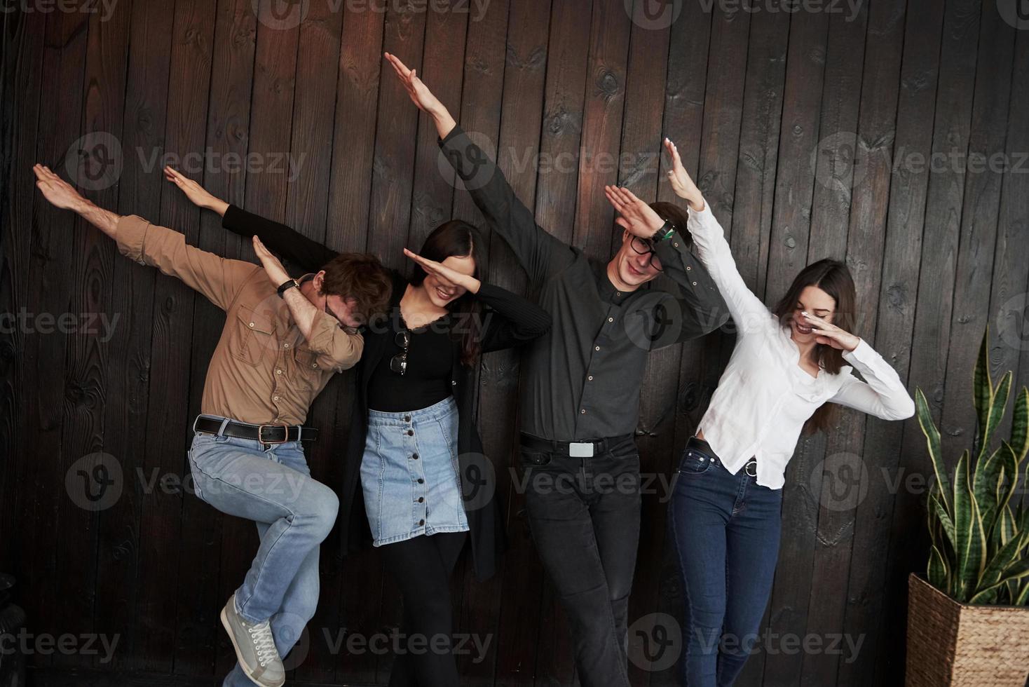 Hands up and to the side. Youth stands against black wooden wall. Group of friends spending time together photo