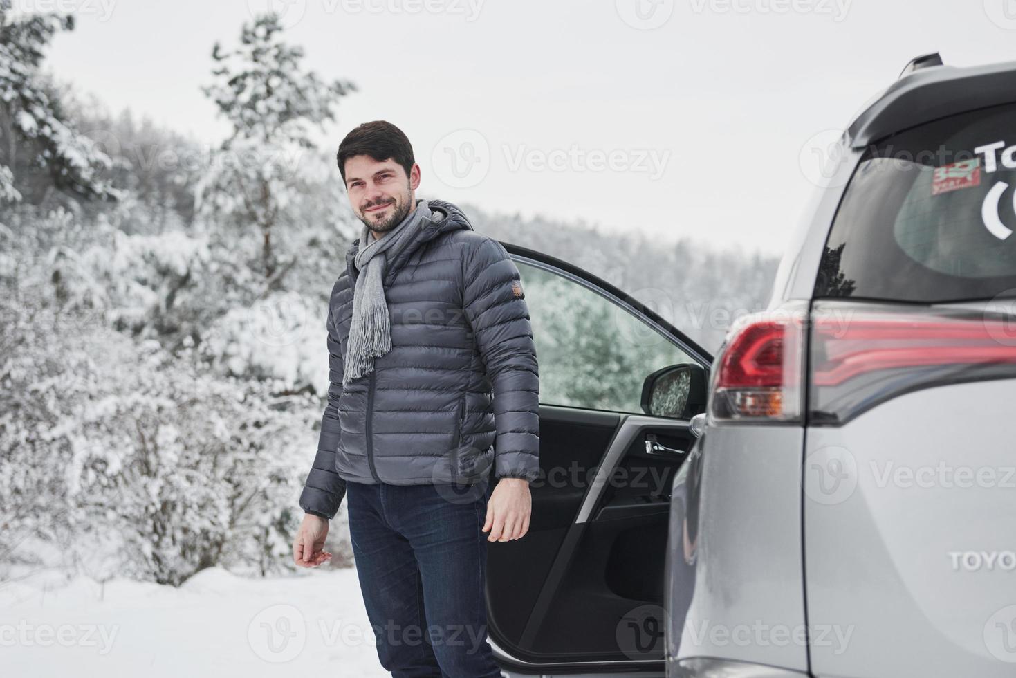 Looking where to go. Guy with long scarf on the neck is walking out from the car to have a walk in winter snowy forest photo