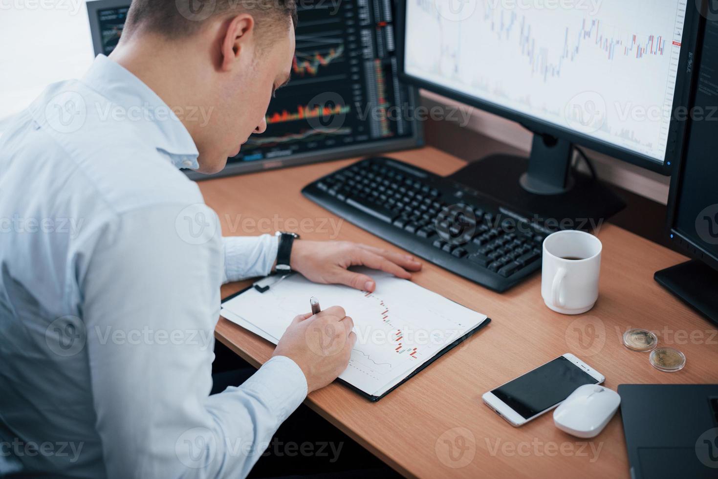 correcciones en los gráficos en papel. hombre que trabaja en línea en la oficina con múltiples pantallas de computadora en gráficos de índice foto