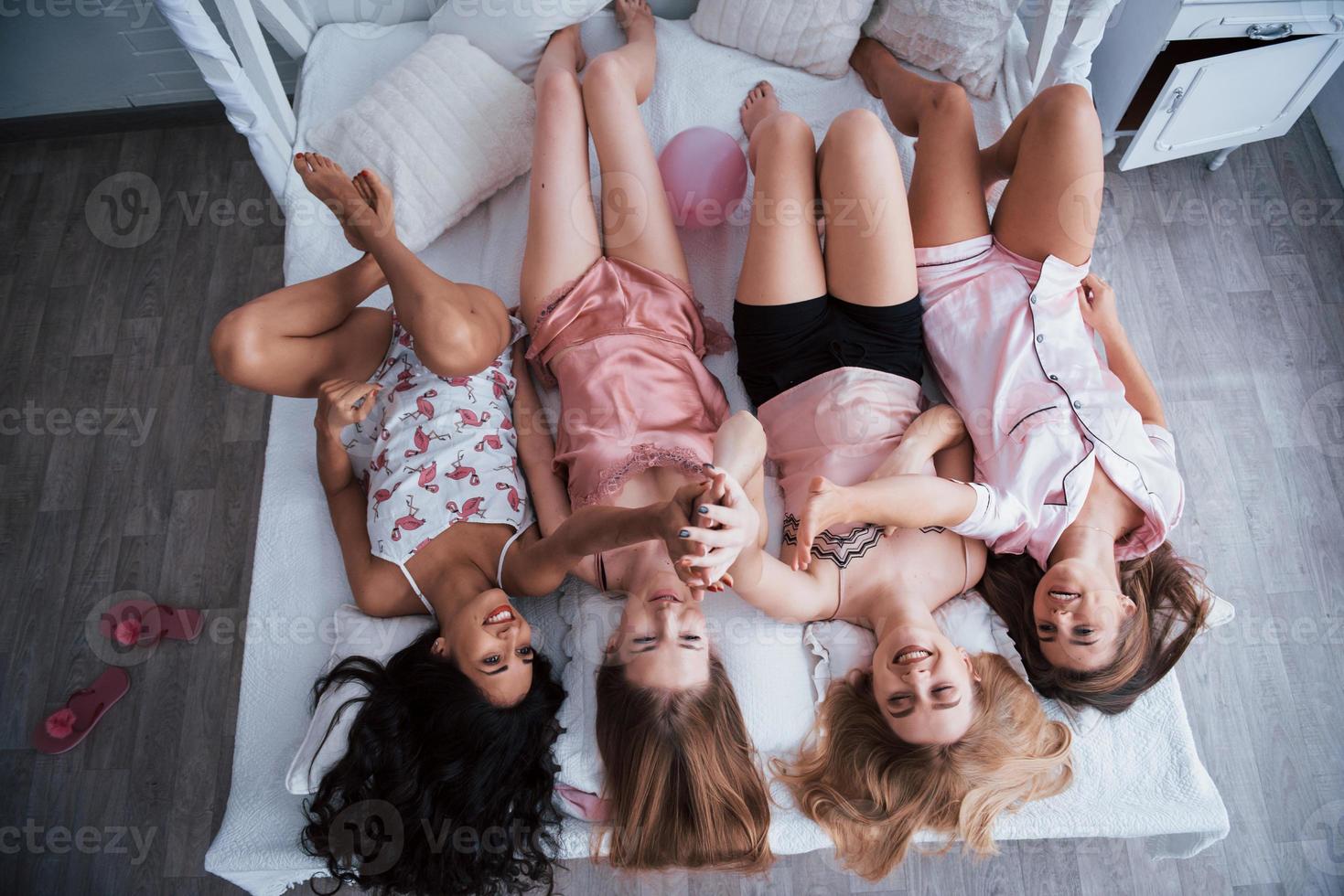 Beautiful hair. Inverted portrait of charming girls that lying on bed in nightwear. Top view photo