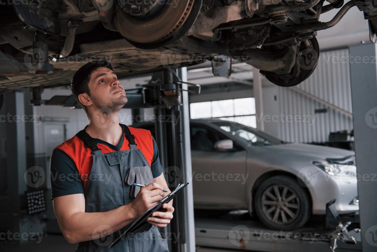 Counting how many details needed. Man at the workshop in uniform using notepad for his job for fixing broken car photo