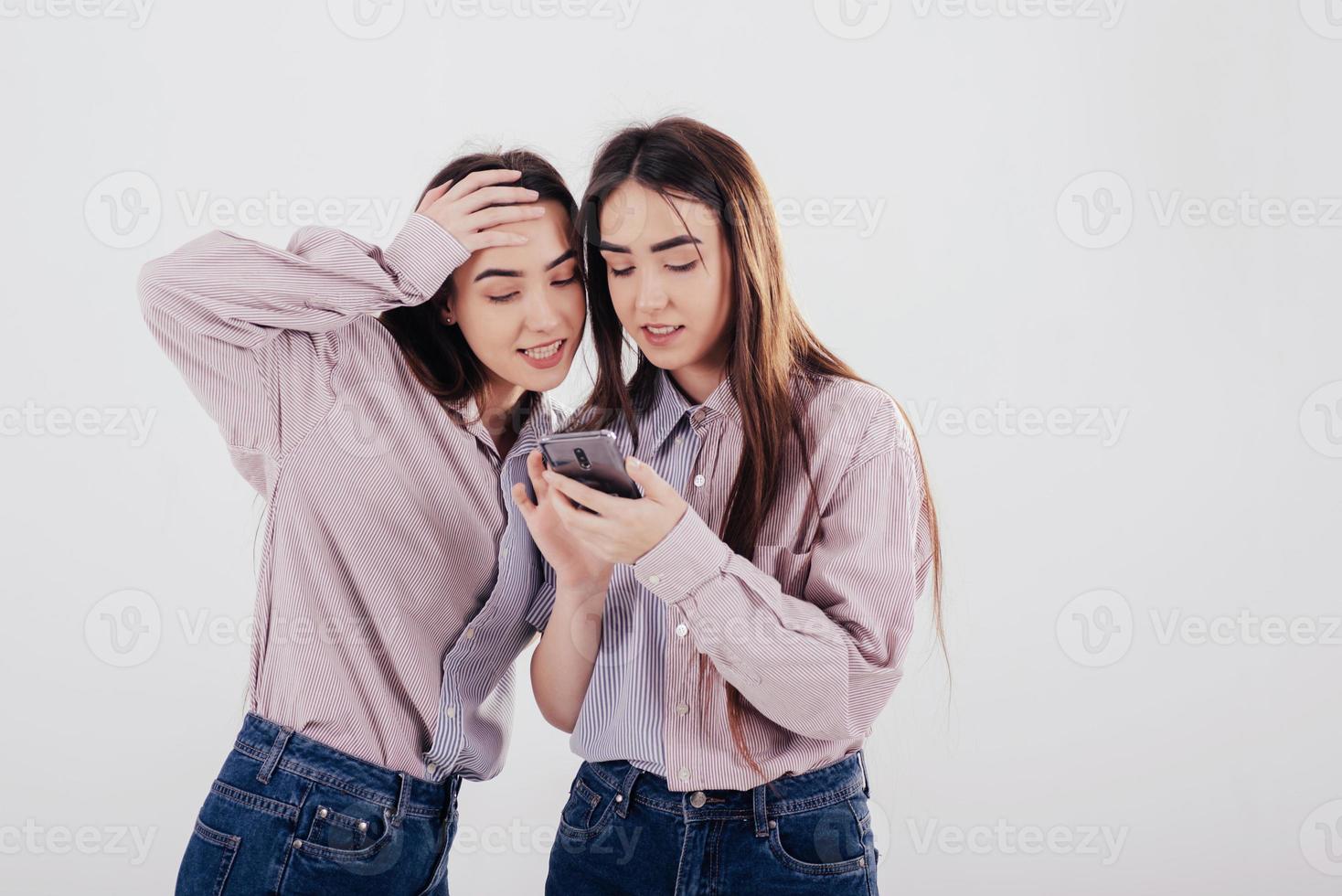 Modern technology. Two sisters twins standing and posing in the studio with white background photo