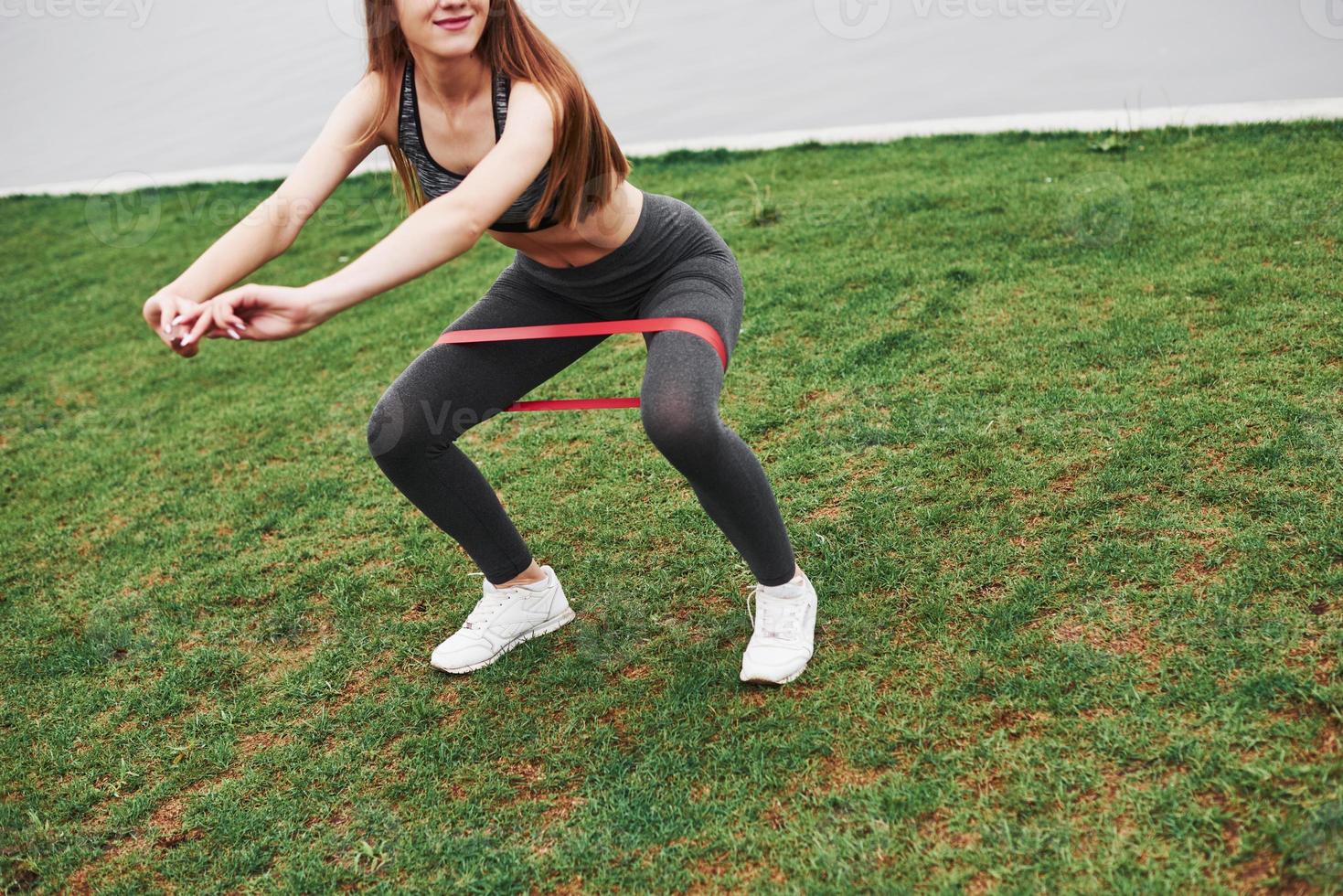 Young blonde have workout outdoors on the green grass near the water photo