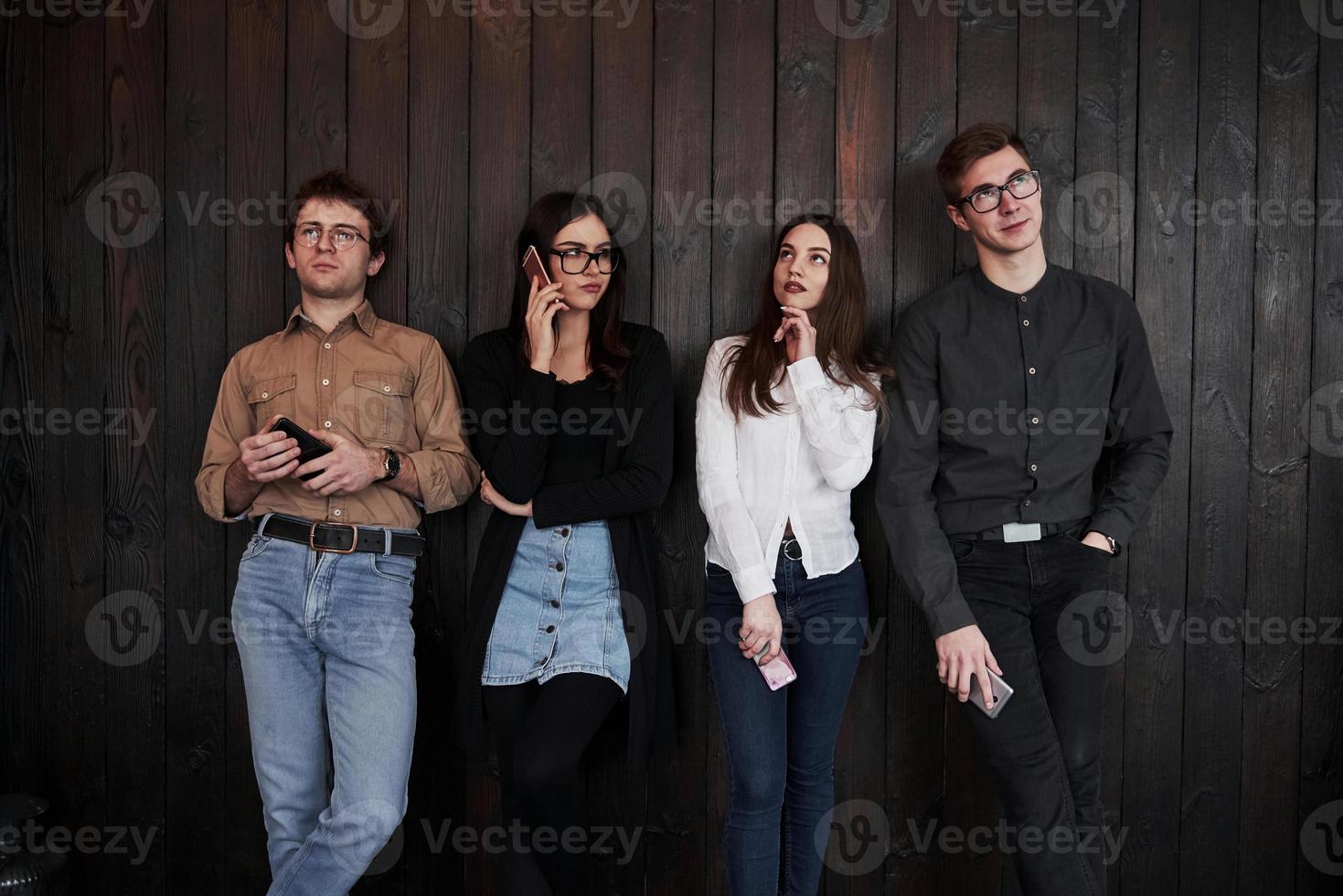 Everyone looks in different directions. Youth stands against black wooden wall. Group of friends spending time together photo