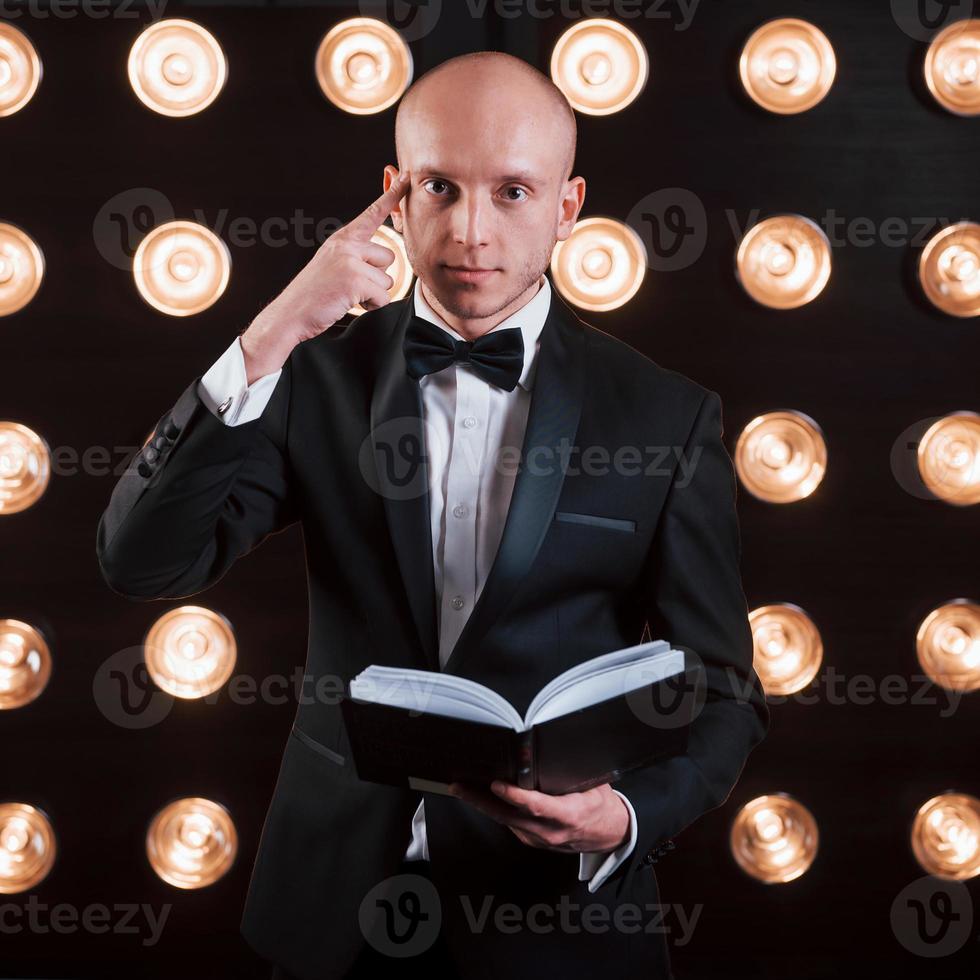 He know what you thinking about. Magician in black suit standing in the room with special lighting at backstage photo