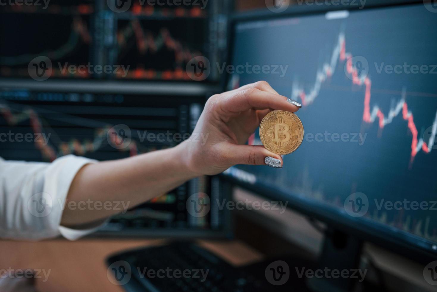 Exchange conception. Woman's hand holding bitcoin in modern office with many monitors with graphs photo