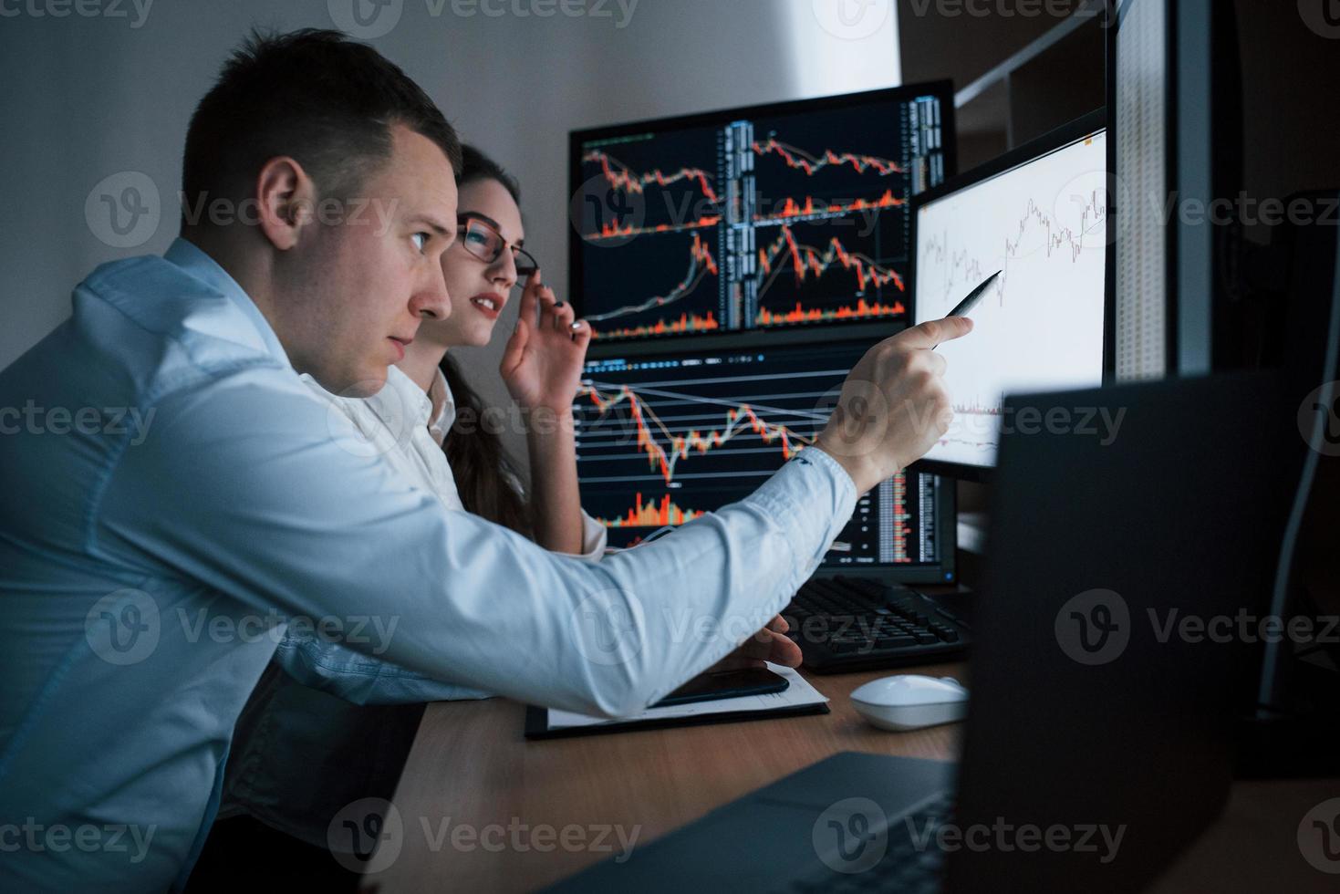 Pay attention to this point of time. Team of stockbrokers are having a conversation in a office with multiple display screens photo