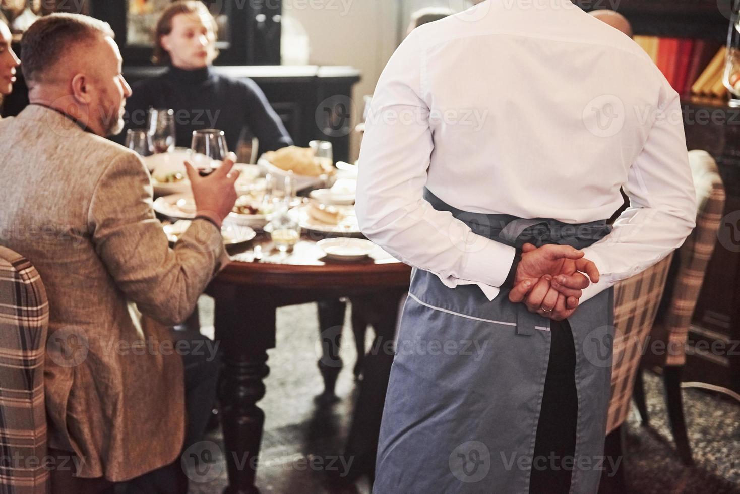 de la parte de atrás del camarero. amigos de la familia pasando un buen rato en un hermoso y lujoso restaurante moderno foto