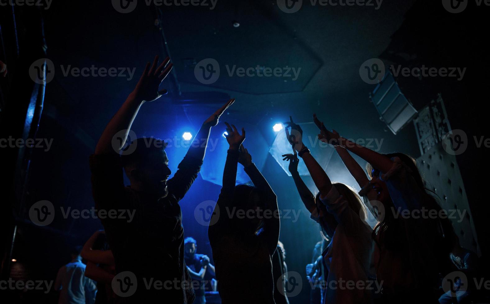 con los brazos levantados. grupo de personas que disfrutan bailando en la discoteca con hermosas luces foto