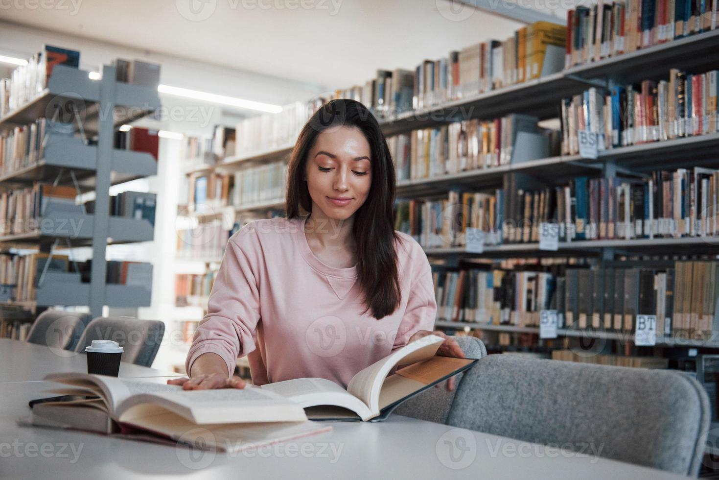 Calm and quiet. Brunette girl in casual clothes having good time in the library full of books photo