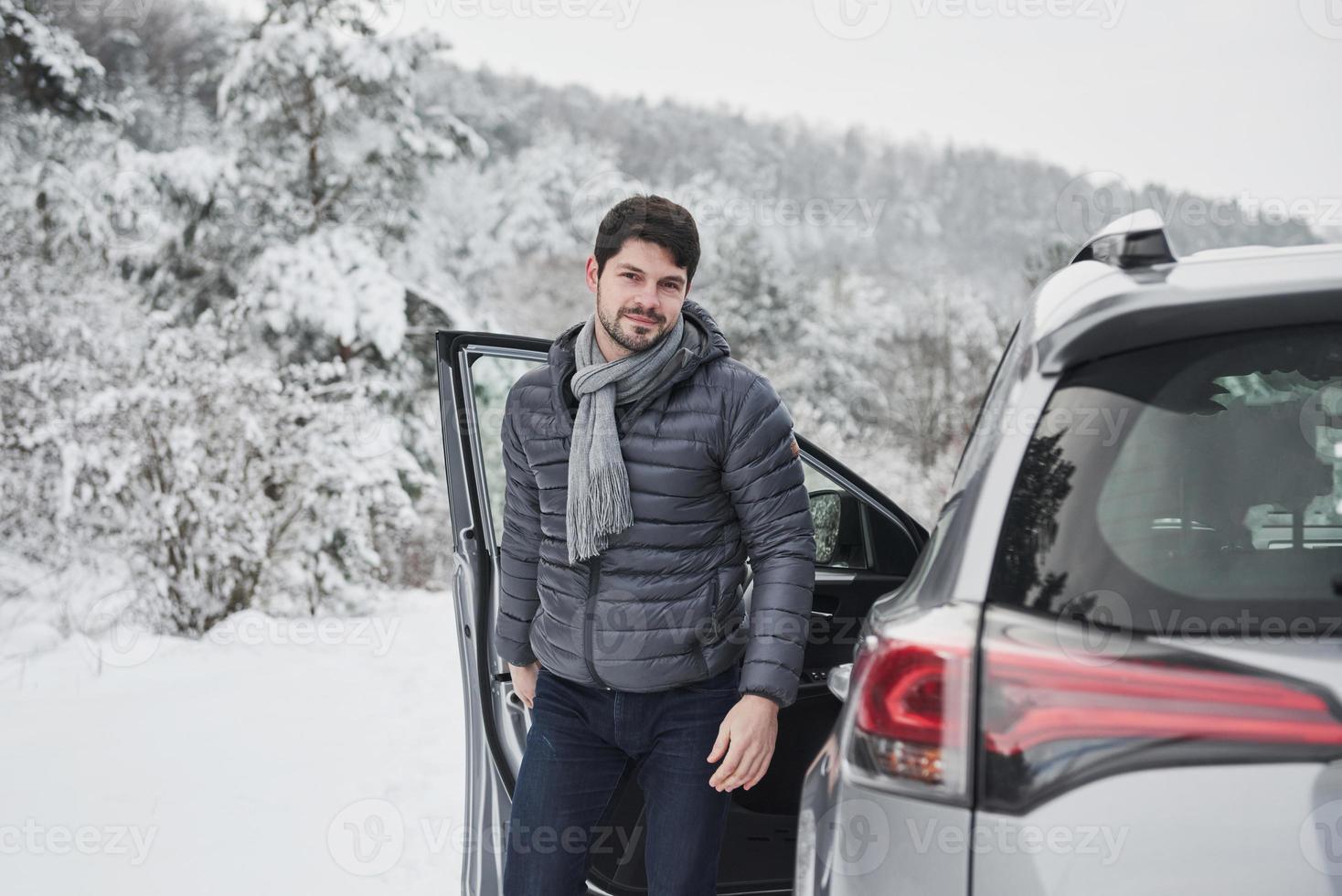 Guy with long scarf on the neck is walking out from the car to have a walk in winter snowy forest photo