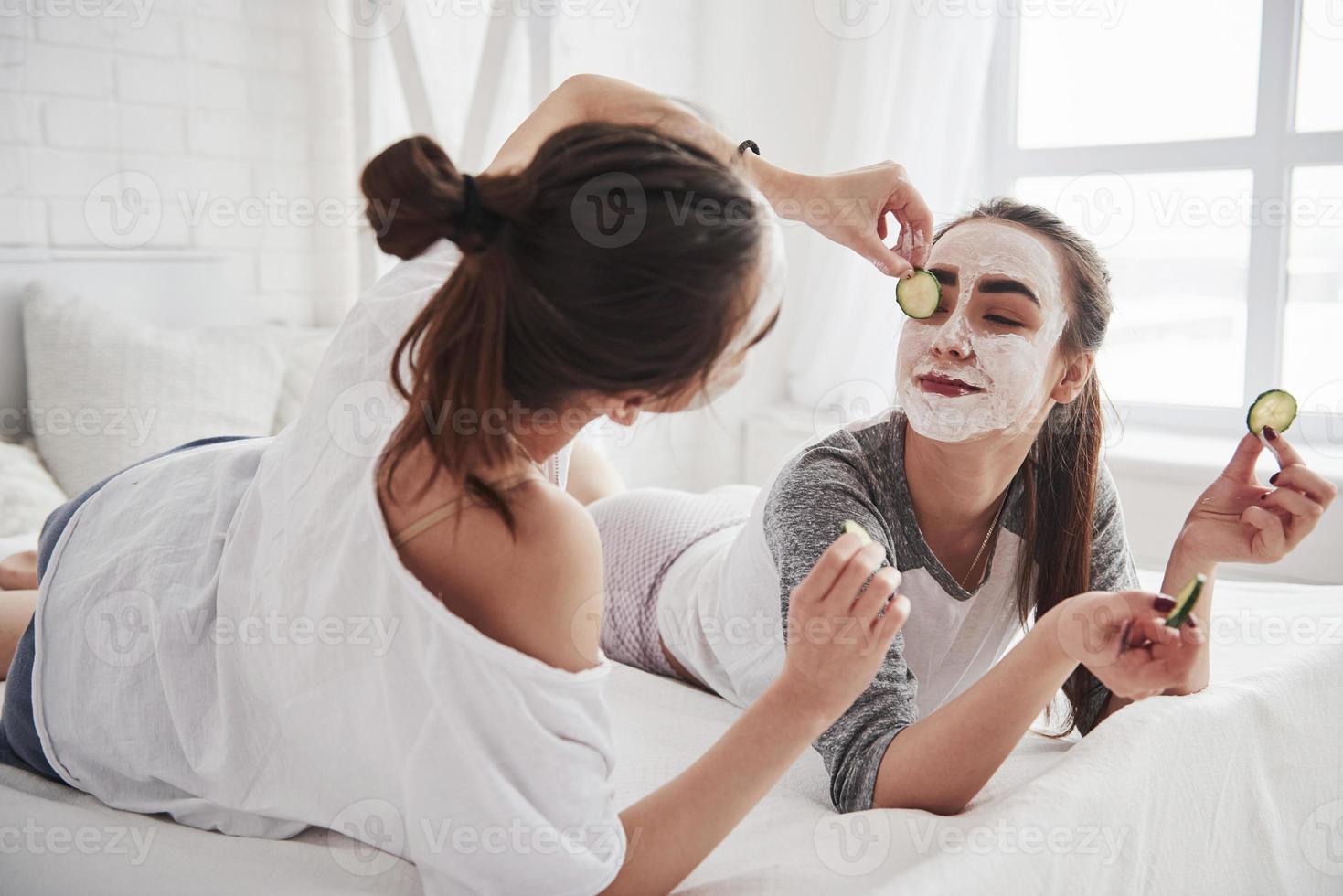 That's will look great on you. Conception of skin care by using white mask and cucumbers on the face. Two female sisters have weekend at bedroom photo