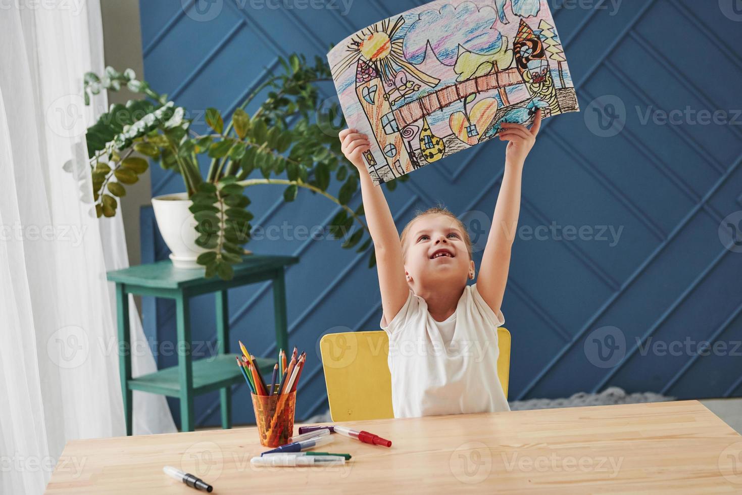 Look at my masterpiece. Cute little girl in art school shows her first paintings drawn by pencils and markers photo
