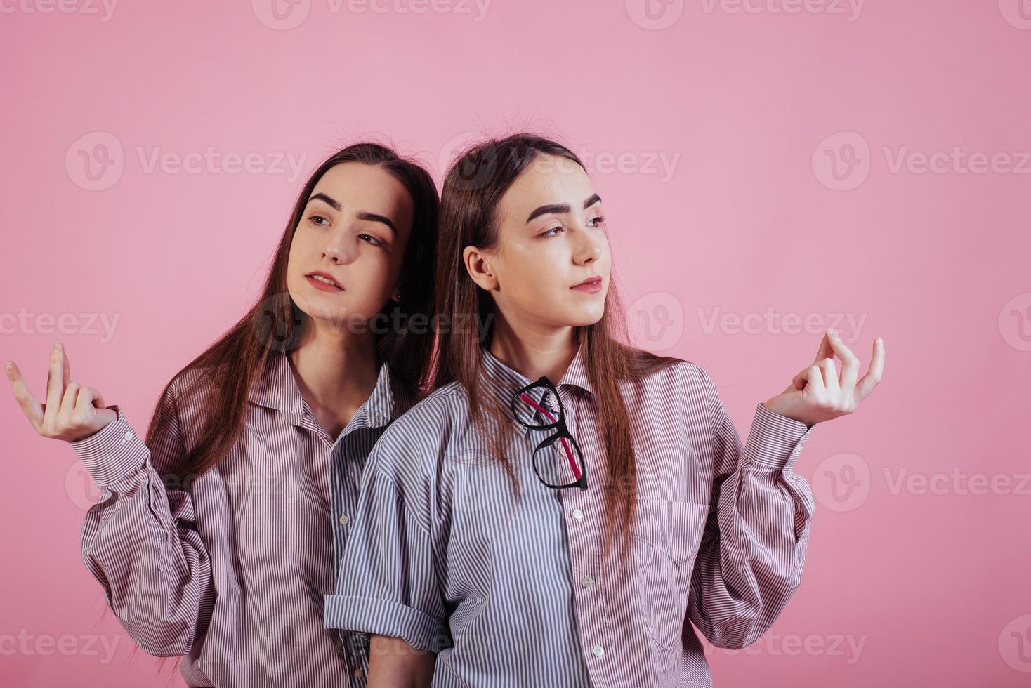 Looking to the sides. Two sisters twins standing and posing in the studio with pink background photo