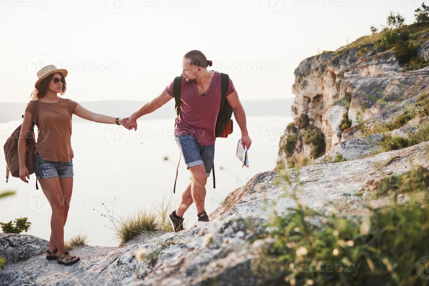 Two tourist male and woman with backpacks climb to the top of the mountain and enjoying sunrise. Travel lifestyle adventure vacations concept photo