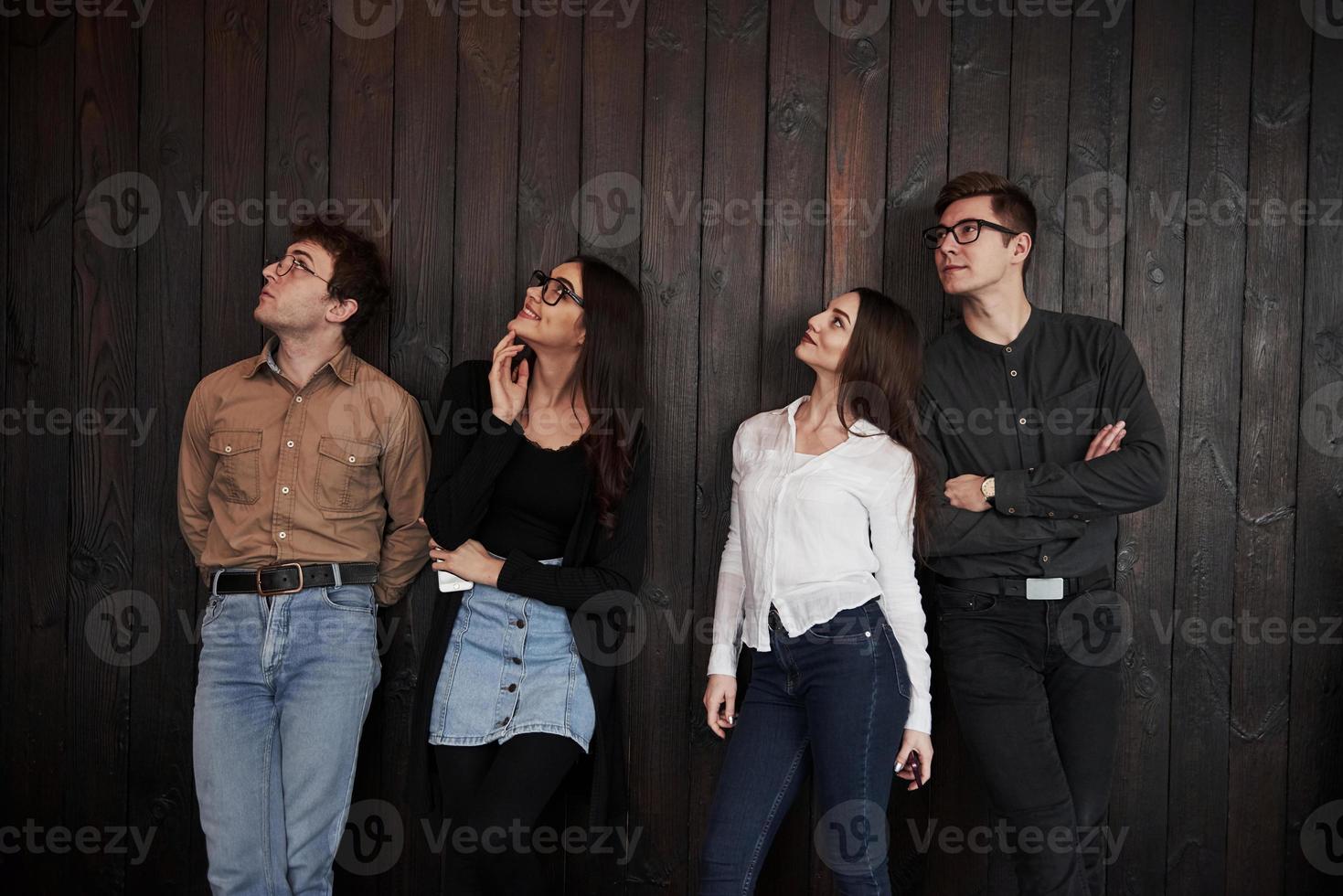 What's that up there. Youth stands against black wooden wall. Group of friends spending time together photo