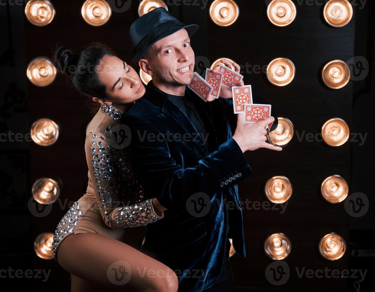 Girl is huggng her man while he showing tricks with cards. Happy couple posing for the portrait. Family business of magician tricks and shows photo