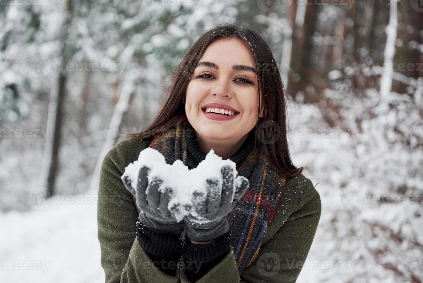 Happy brunette holding snow in hands and smiling. Winter forest photo