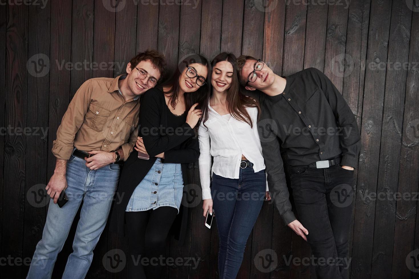 relajado y feliz. el joven se para contra la pared de madera negra. grupo de amigos pasando tiempo juntos foto