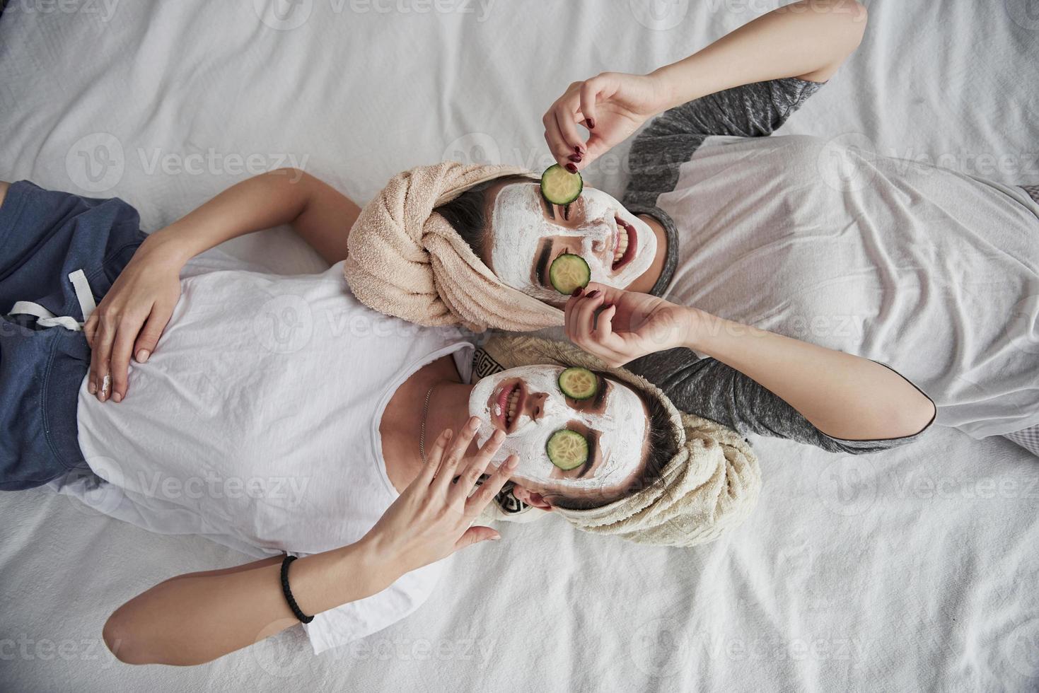 Taking off these things. Lying on the white bed. Top view. Conception of skin care by using white mask and cucumbers on the face photo