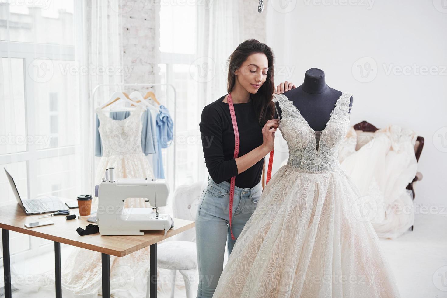 imagina cómo le sentará a la novia. diseñadora de moda femenina trabaja en la ropa nueva en el taller foto