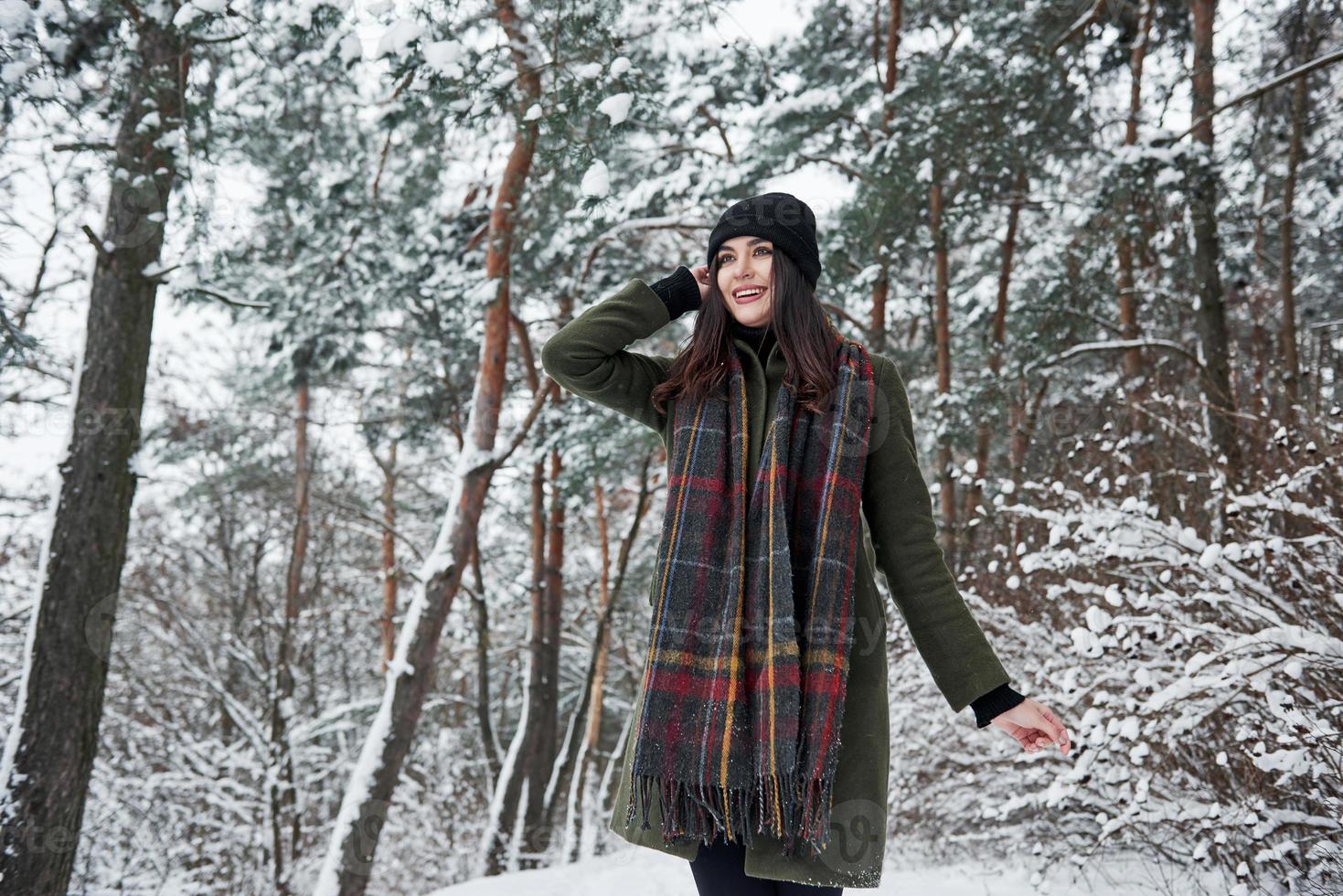 Long scarf. Cheerful young girl in warm clothes have a walk in the winter forest at daytime photo