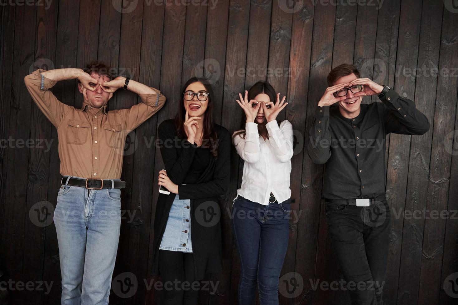 Making gestures. Youth stands against black wooden wall. Group of friends spending time together photo