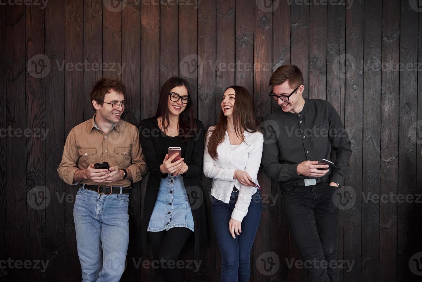 tener una conversación el joven se para contra la pared de madera negra. grupo de amigos pasando tiempo juntos foto