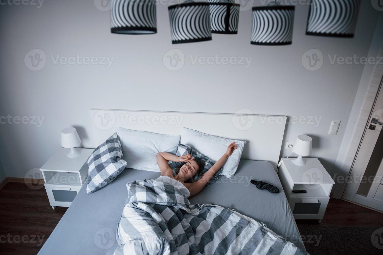 Stylish room. Woman with blindfold mask for a sleep is lying on the bed at morning time photo