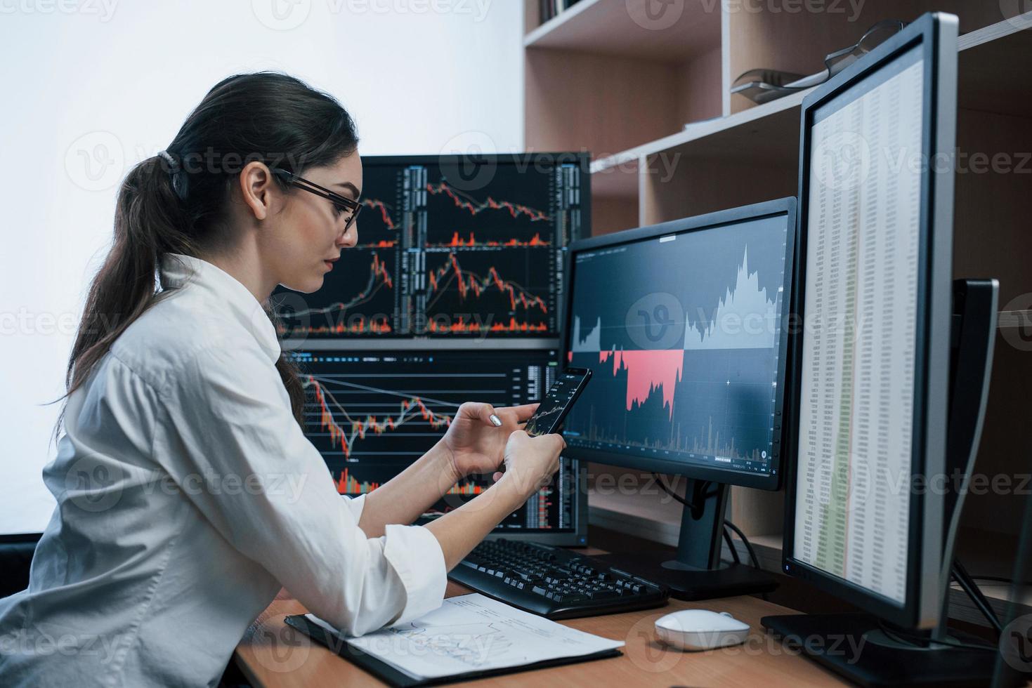 Gorgeous brunette. Woman working online in the office with multiple computer screens in index charts photo