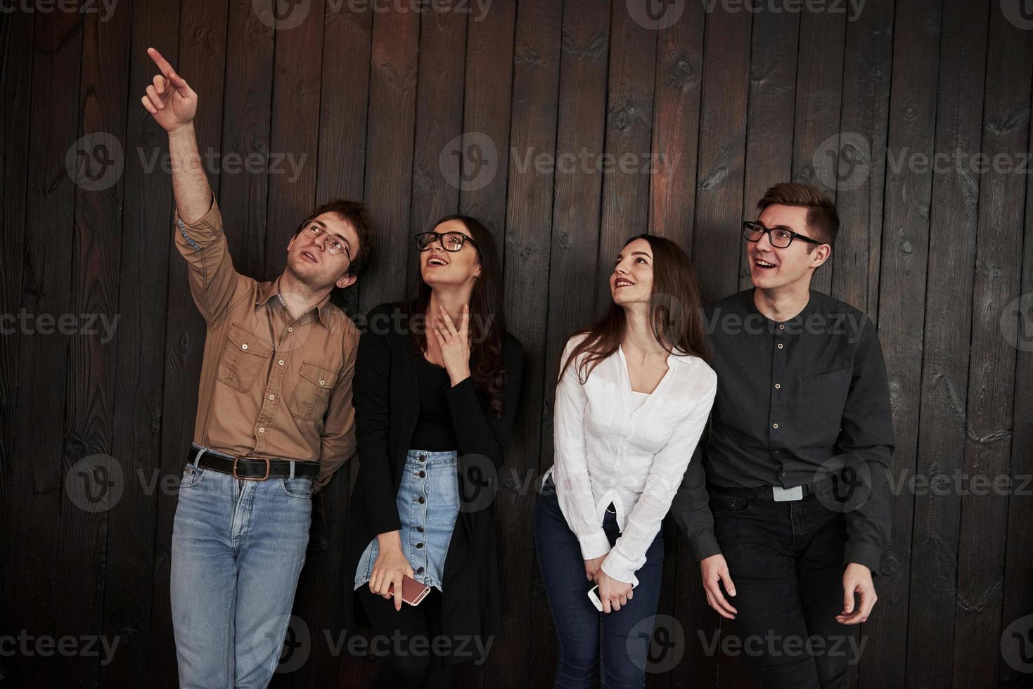 mira esa decoración. el joven se para contra la pared de madera negra. grupo de amigos pasando tiempo juntos foto