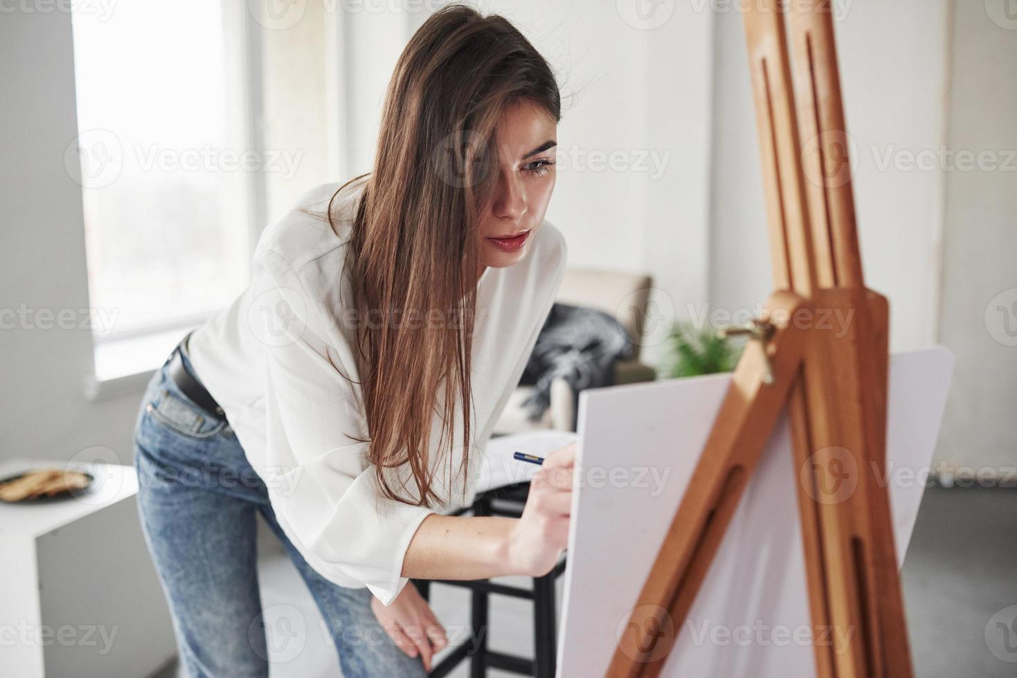 The process of drawing. Young brunette in the room with white walls and daylight that comes from the window photo