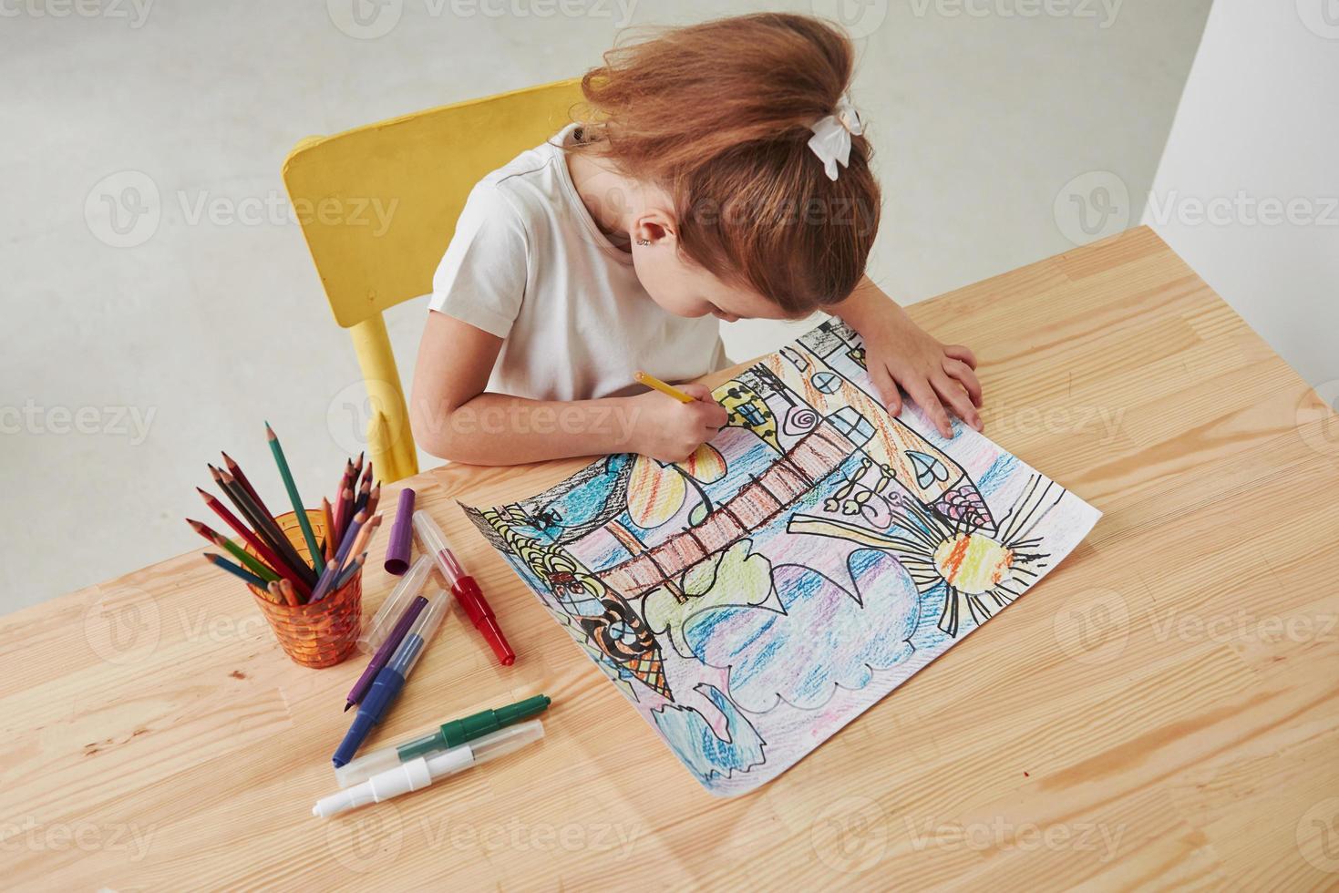 View from the top. Cute little girl in art school draws her first paintings by pencils and markers photo